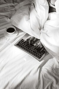 Entrepreneur typing on laptop in bed with coffee