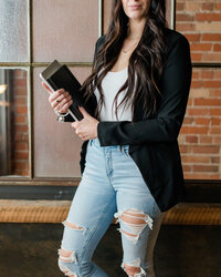 Cropped detail of Allie Clark holding black notebooks while dressed in a black blazer and distressed jeans, symbolizing her blend of strategy and creativity at Allie Clark Designs.