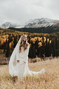 bride standing in a field with mountains in the background