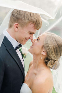 Husband and Wife touching noses smiling at each other while looking into each others eyes under a veil