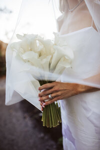Bride holding a white calla lily   bouquet in soft evening light during her Maine wedding.