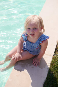 An adorable little girl sitting by the pool, radiating charm and innocence in the sunshine
