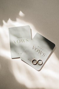 Two wedding bands sit on a wedding stationary spread in the sun