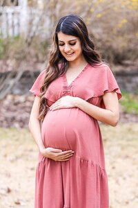 Mom to be in a rose pink maternity dress holding her baby bump while smiling down at her unborn child