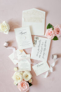 invitation flatlay on a pink background decorated with florals and ribbon
