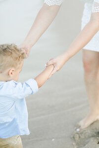 mother and son hand in hand on the beach beach photoshoot light and airy edit toddler beach curly golden blonde hair golden hour