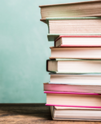 Nine books are stacked with their leaf edges displayed. They are sitting on a wooden desk.