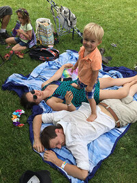 Candid shot of Tarzan and her husband lying in the grass on top of blankets, a small boy stands on top of them, one foot on each of his parents