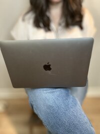 Cropped image showing a woman’s crossed legs in blue jeans with a silver laptop resting on her lap.