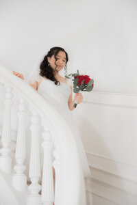 Bride descending stairs holding bouquet of roses