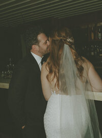 groom whispering into brides ear at the bar