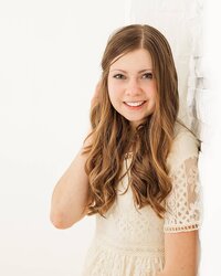 Girl smiling and holding her hair by a white wall in a white indoor studio in North East, PA.