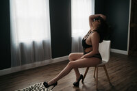 Brunette woman sitting on white chair wearing black lingerie in Boston Boudoir photographer Kerry Callahan boudoir's studio