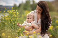 Bright and cheerful portrait of a mother with long brown hair holding her toddler son while immersed in yellow flowers in the springtime. Portrait by Brittany Danielle Photography.
