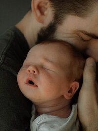 Father snuggling his newborn baby in soft natural light during a lifestyle newborn session in Riverside County.