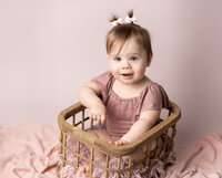 one year old girl in pink sitting in basket for cake smash session