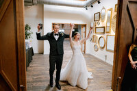 Bride and groom throw their hands up and cheer as they enter the wedding reception