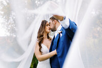 bride and groom under the veil kissing as he holds the veil, captured by Minnesota wedding photographer.  
