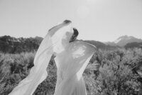 black and white photo of bride with long flowy sleeves holding them up to face