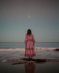 Woman in pink dress walking beach at golden hour during solo reflection