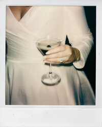 A polaroid photo of a bride holding a wine glass in her ring hand