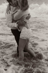 Black and white engagement photo of couple kissing while standing in the ocean