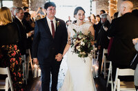 A newlywed couple holding hands and walking back up the aisle 