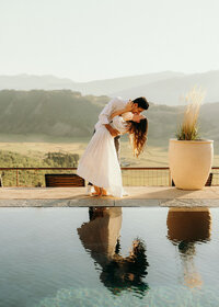 man and woman standing by a poll kissing with mountains in the background