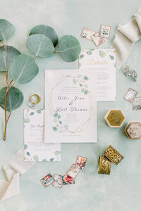Wedding invitation and wedding detail flatlay in dusty sage, warm neutral tones, gold, and pops of pink