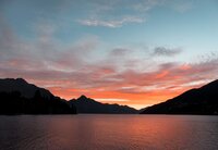 Orange pink sun setting over dark mountains in front of a lake