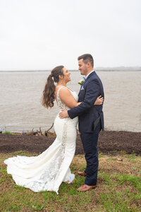 Bride and groom smiling at each other with a river and dirt behind them in Richmond, Virginia.