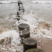 Ocean waves splashing against a wooden groyne, symbolizing stability, flow, and the natural rhythm of transformation in a coastal wellness setting.