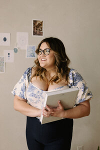 Wedding planner, Zelie & Co., smiling and looking to the side with a planning book in her hands.
