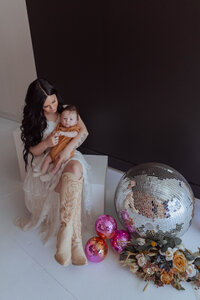 Mother cuddling newborn on modern props in photography studio all white