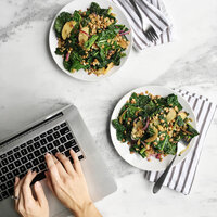 Woman visiting the Eat Your Nutrition website on her computer with a plate of healthy food.