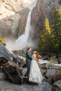 A bride and groom laughing in the waterfall mist during their Yosemite elopement.