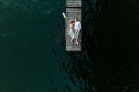 Drone engagement photo of a couple laying on a dock surrounded by water