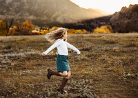 Girl twirling in a field in Colorado at sunset for fall family photos