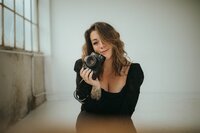 Jaime, a Washington wedding and elopement photographer, smiling and holding a film camera for her About page portrait.