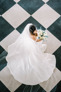 Photo from above of a bride with her dress train spread out over a black and white tile floor