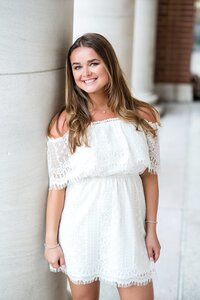 Woman leaning against pillar wearing a white dress