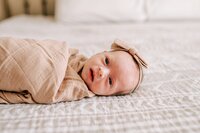 Newborn baby girl with a bow laying on a bed in Orlando
