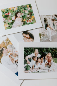Four printed photographs with white mat lay on table together, showing printed photos of a young family with two children