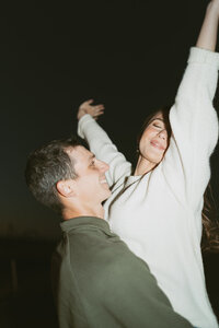 A couple in focus, holding their wedding rings away from their bodies as they lean in for a kiss, creating a romantic and timeless scene.