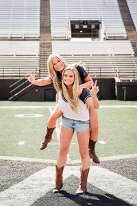 Two senior girls on the Vanderbilt football field in campus shirts, boots, and cute jeans.