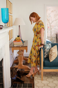 Chelsey Heslop in a yellow pattern dress leaning against the arm of a blue chair