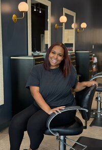 Headshot of SCENE Salon hairstylist and colorist, Marilyn, sitting in salon chair inside SCENE Salon's moody, chic, modern salon space.