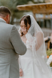 A photo of a bride crying tears of joy while her groom is reading his vows to her.