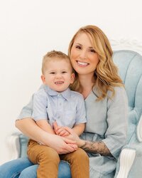 Mother sitting with her son in a blue Victorian chair in an Erie County indoor studio.