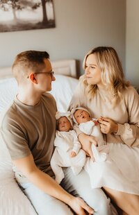 Newborn baby at home, on a bed with mom and she is showering the baby with kisses on her precious cheeks. The are both on a cozy bed with pillows and a soft blanket.